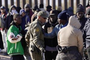 A member of U.S. Customs and Border Protection tries to control a group of migrants.