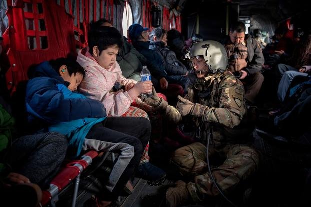 Alaska Army National member passes a bottle of water to a child.